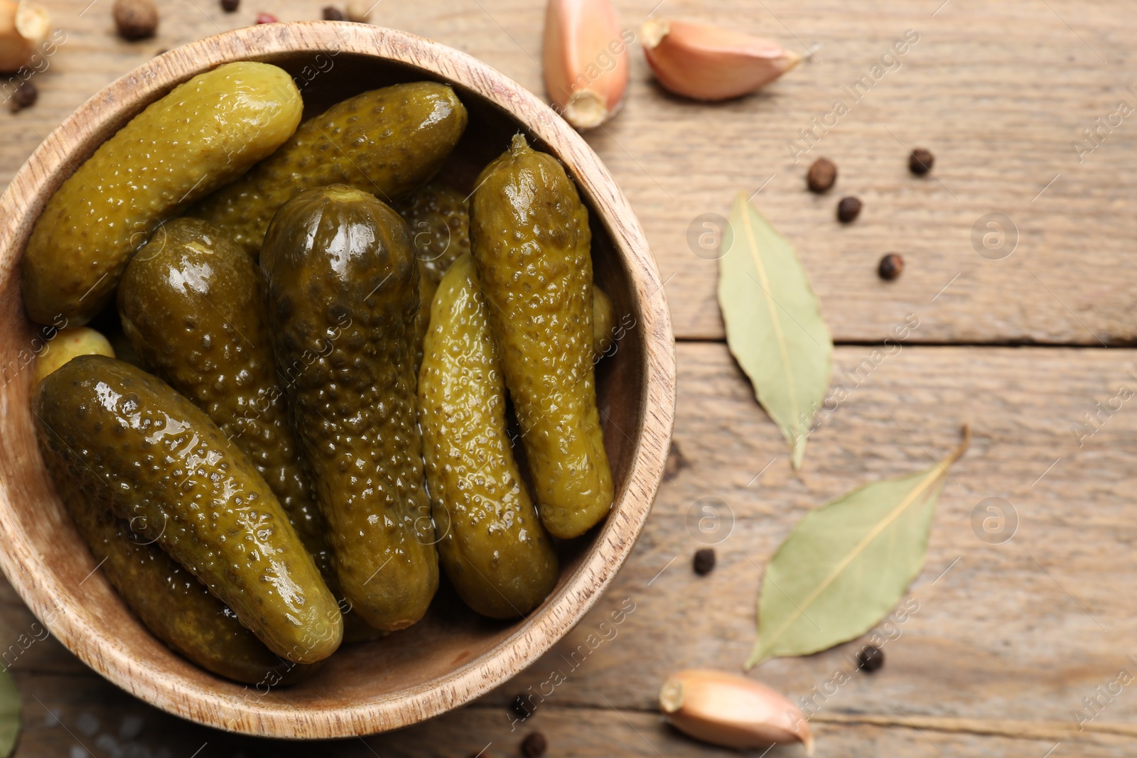 Photo of Tasty pickled cucumbers in bowl on wooden table, top view. Space for text