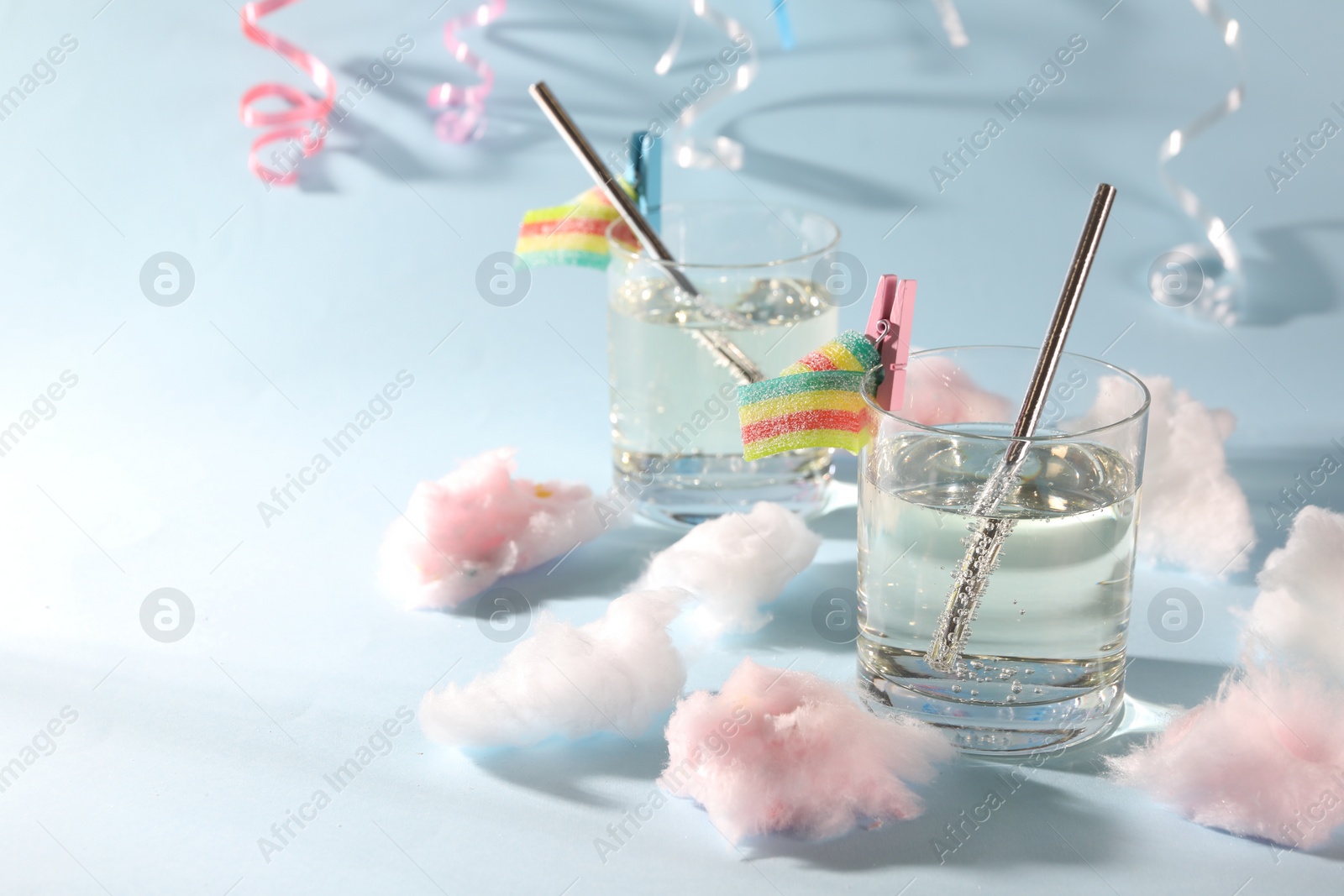 Photo of Tasty cocktails in glasses decorated with gummy candies and cotton candy on light blue background, space for text