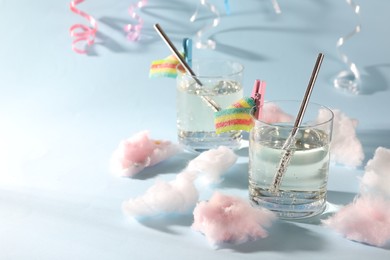Tasty cocktails in glasses decorated with gummy candies and cotton candy on light blue background, space for text