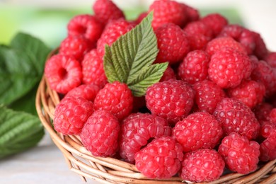 Photo of Tasty ripe raspberries and green leaf in basket on table, closeup