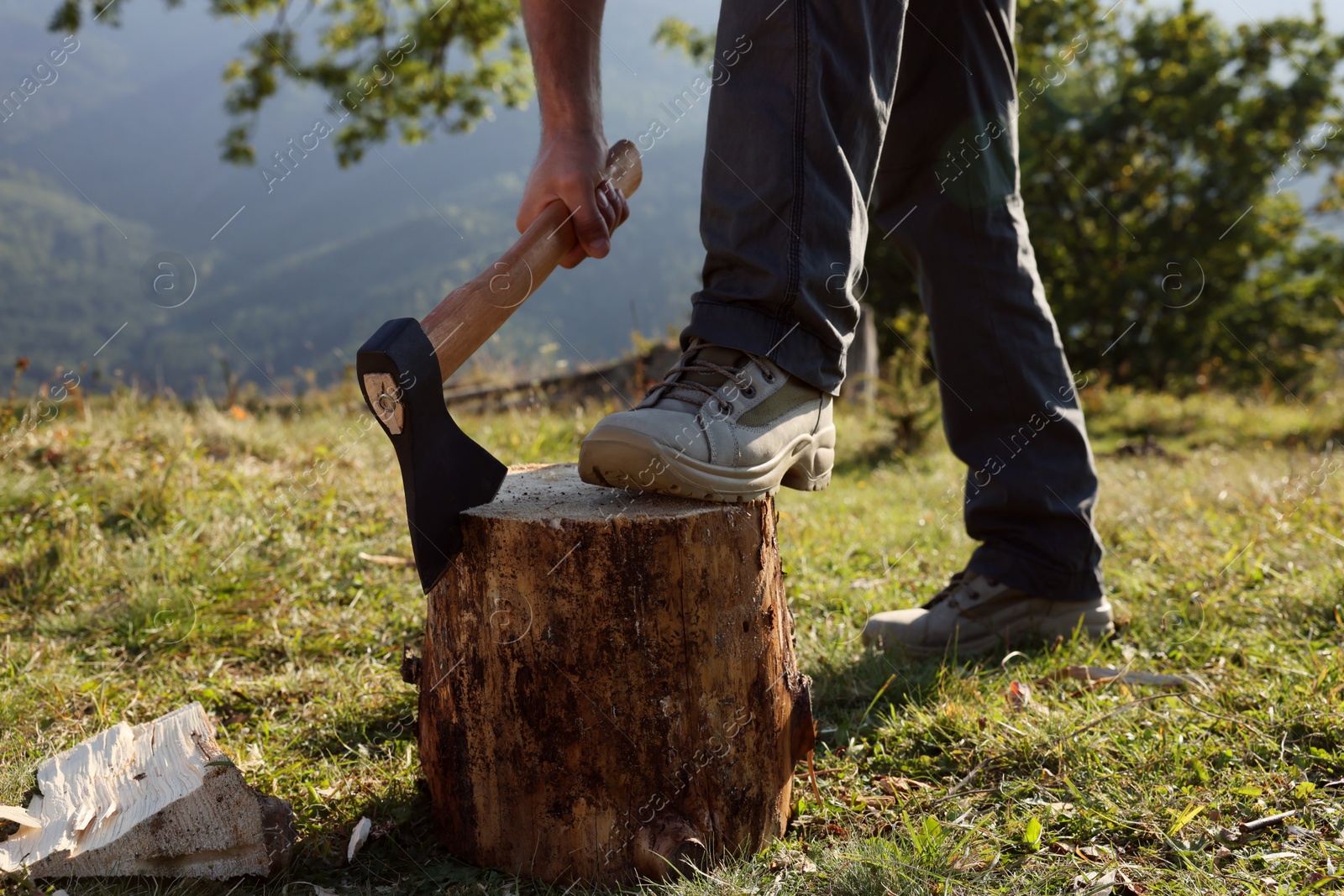 Photo of Man with axe cutting firewood outdoors, closeup