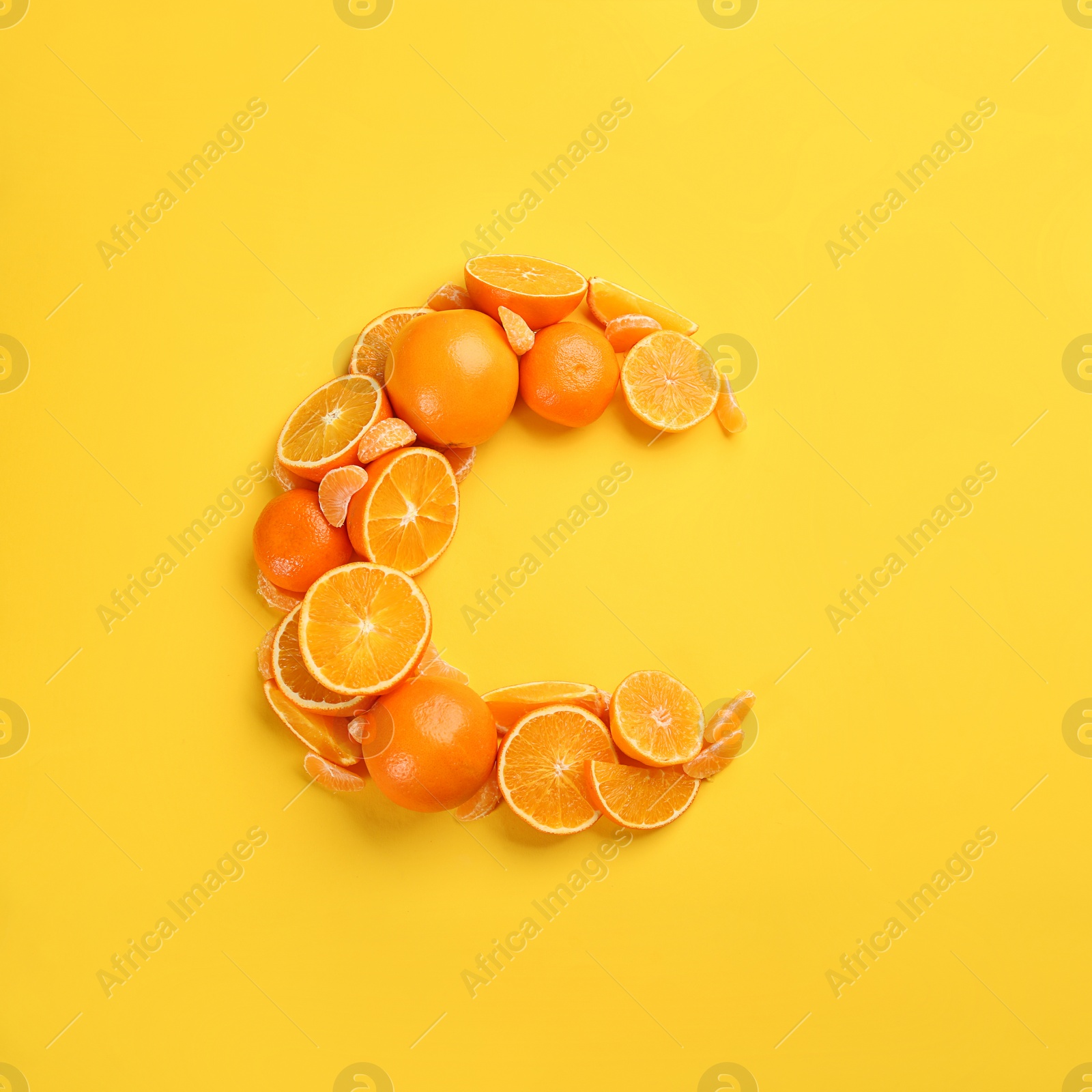 Photo of Letter C made with citrus fruits on yellow background as vitamin representation, flat lay