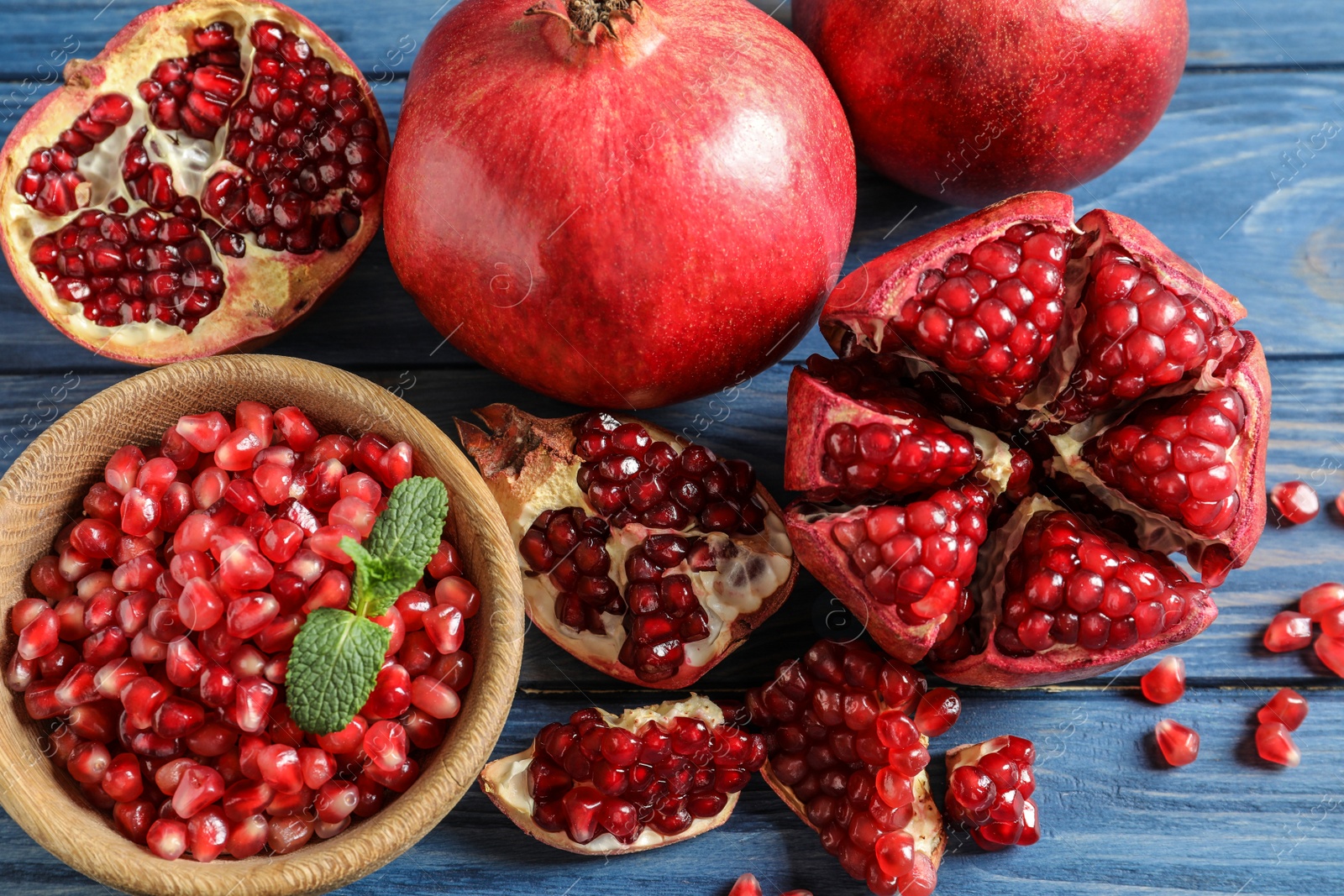 Photo of Bowl with seeds and ripe pomegranates on wooden background, top view