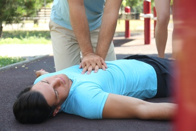 Passerby performing CPR on unconscious man outdoors. First aid