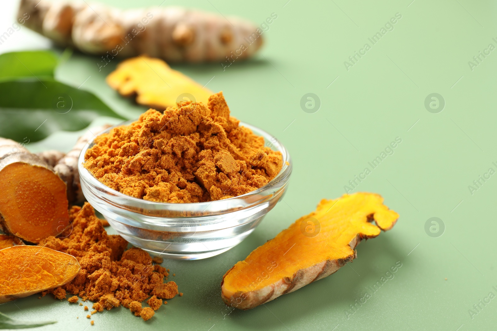 Photo of Aromatic turmeric powder and raw roots on green background, closeup. Space for text