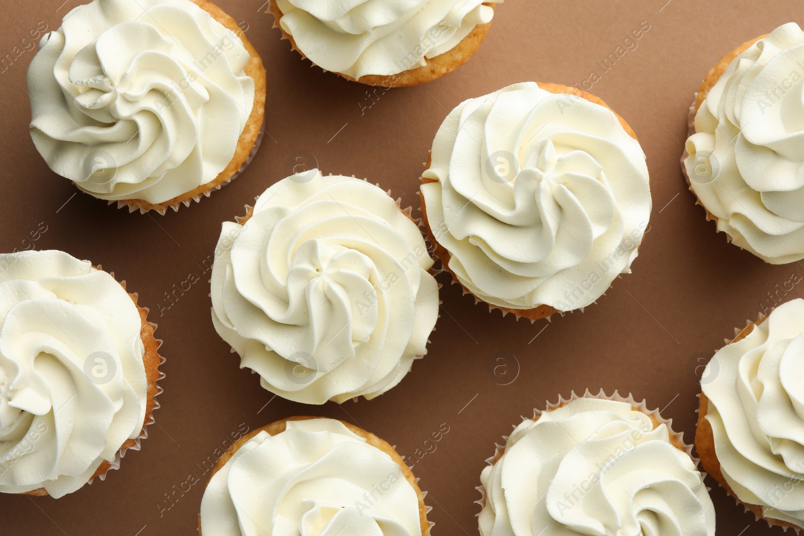 Photo of Tasty vanilla cupcakes with cream on dark beige background, top view