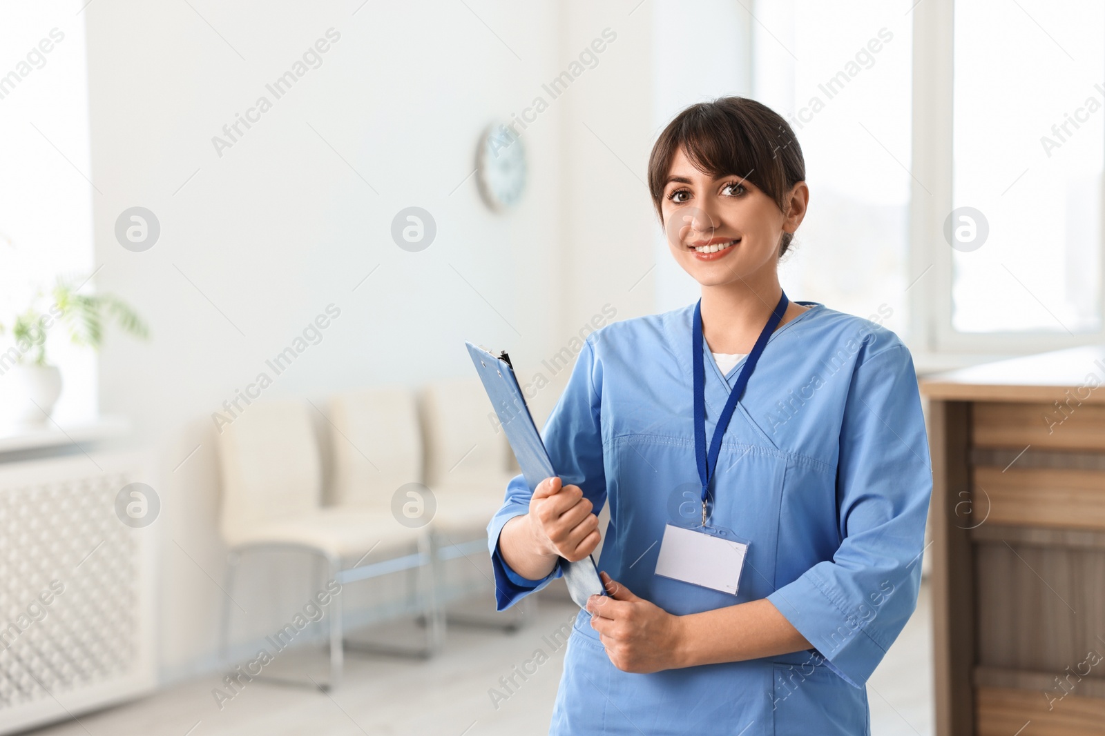 Photo of Portrait of smiling medical assistant with clipboard in hospital. Space for text