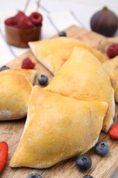 Photo of Wooden board with delicious samosas and berries on wooden board, closeup