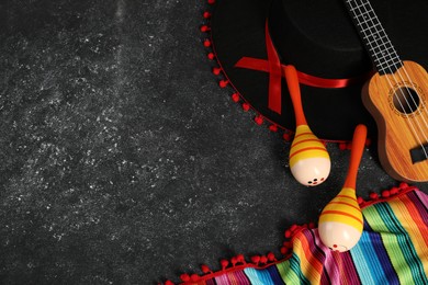 Photo of Black Flamenco hat, ukulele, poncho and maracas on dark textured table, flat lay. Space for text
