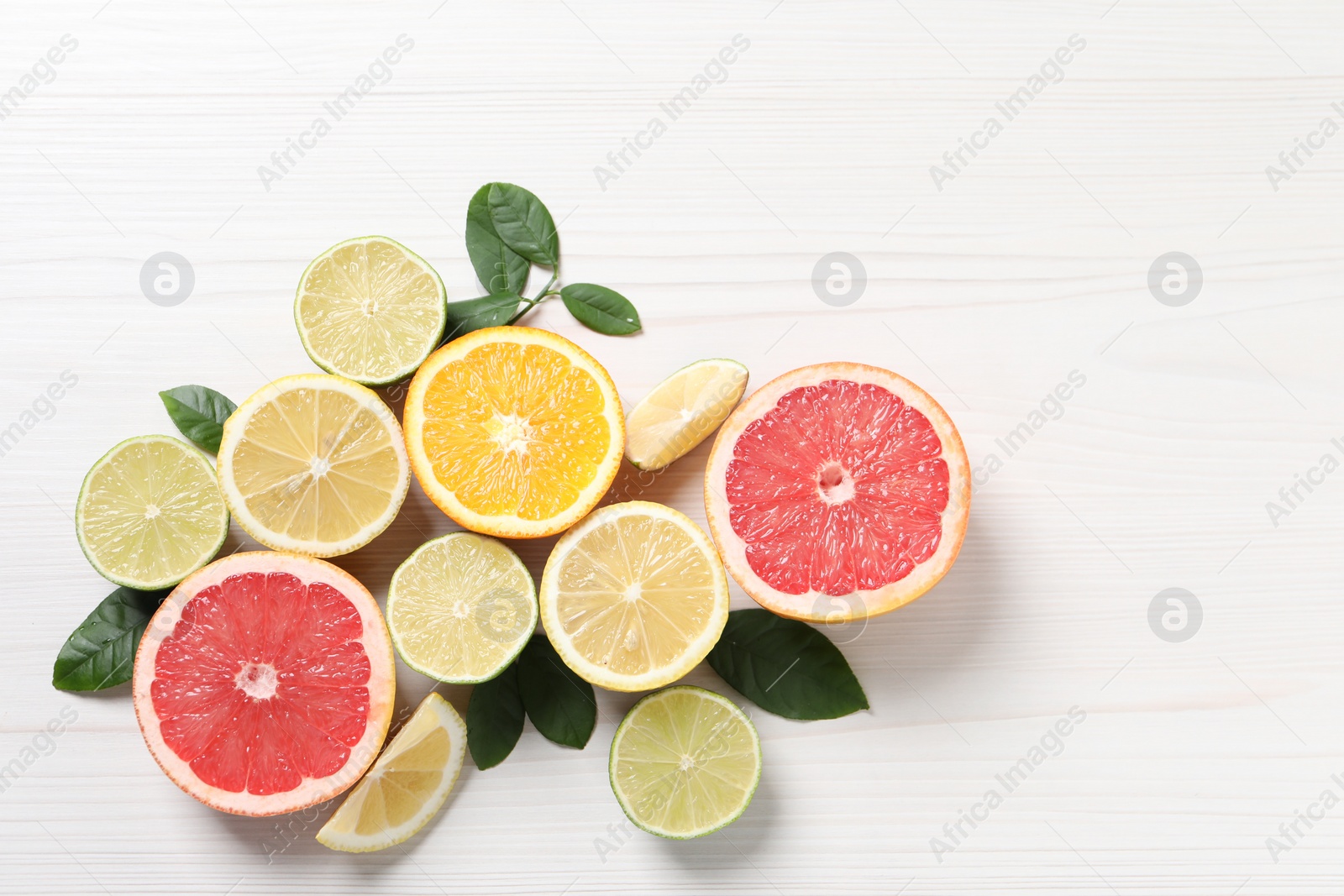 Photo of Different cut citrus fruits and leaves on white wooden table, flat lay. Space for text