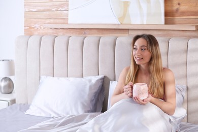 Photo of Young woman holding cup of drink on comfortable bed with silky linens, space for text
