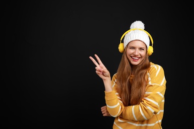 Photo of Young woman listening to music with headphones on black background, space for text