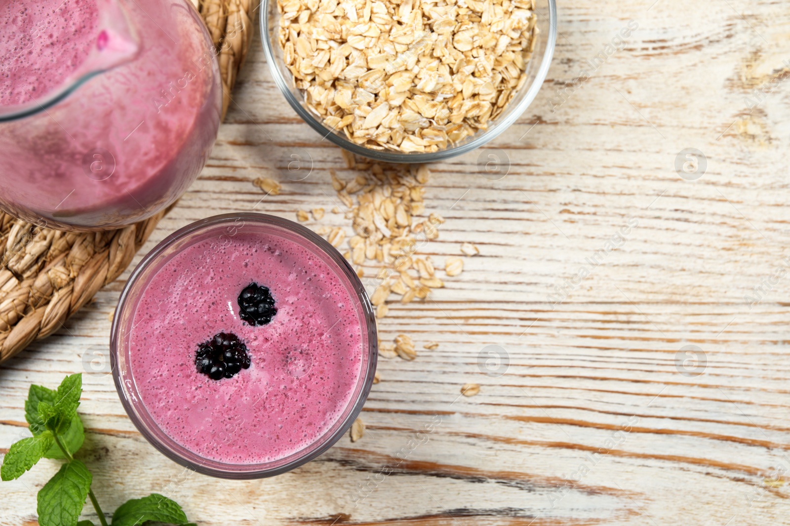 Photo of Glass of blackberry smoothie with mint and oatmeal on light wooden table, flat lay. Space for text