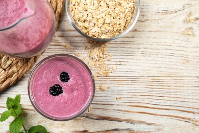 Photo of Glass of blackberry smoothie with mint and oatmeal on light wooden table, flat lay. Space for text