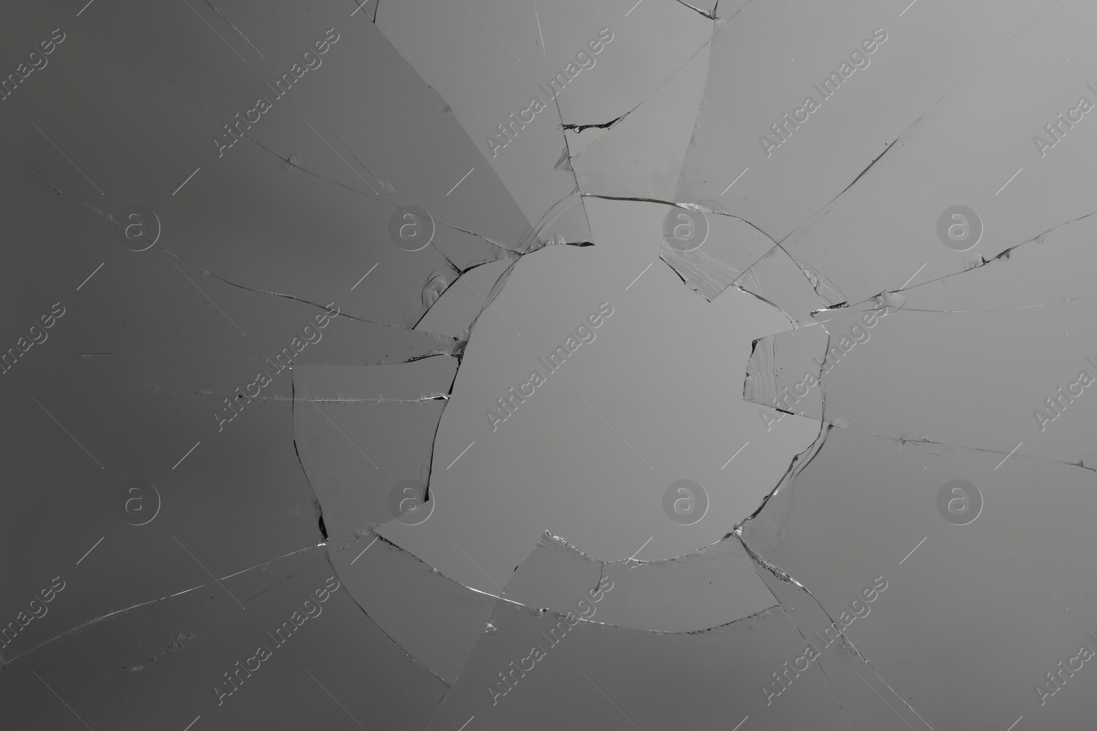 Photo of Closeup view of broken glass with cracks on grey background