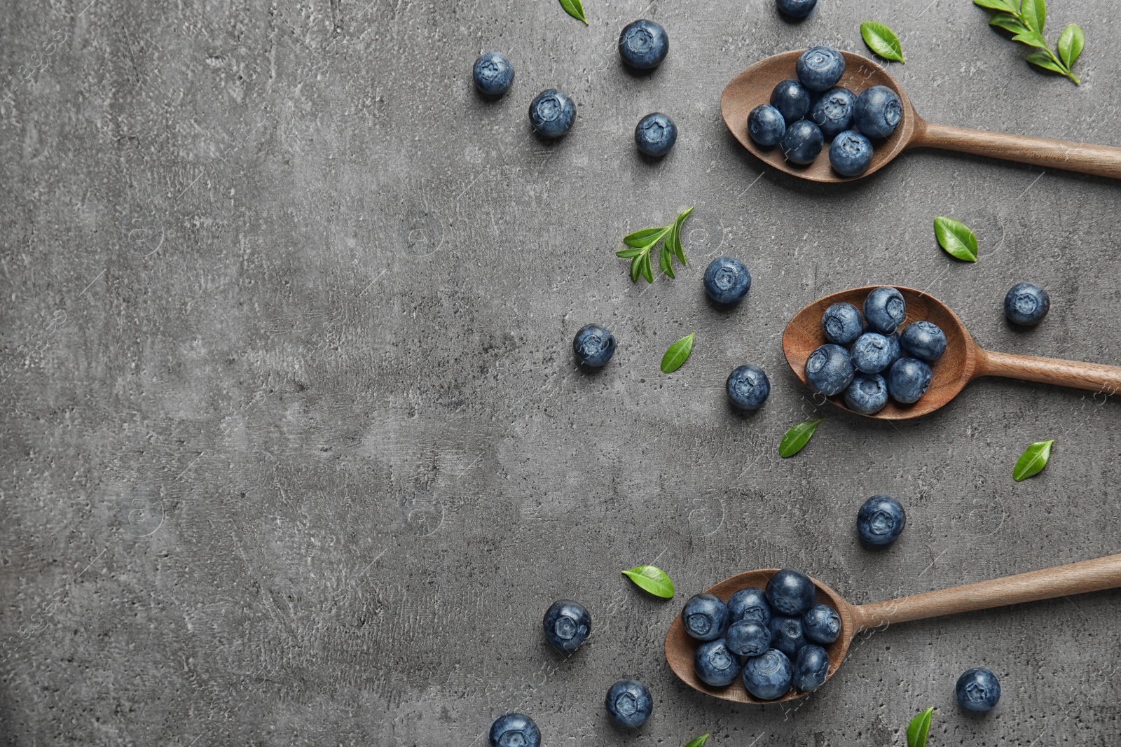 Photo of Flat lay composition of wooden spoons with tasty blueberries and leaves on grey stone surface, space for text