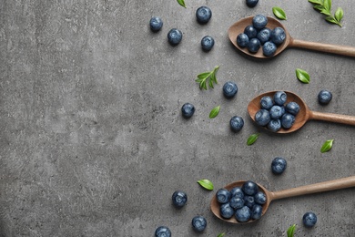 Photo of Flat lay composition of wooden spoons with tasty blueberries and leaves on grey stone surface, space for text
