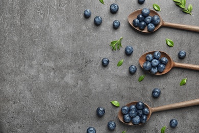 Flat lay composition of wooden spoons with tasty blueberries and leaves on grey stone surface, space for text