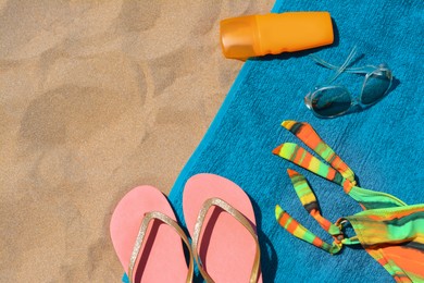 Photo of Soft blue beach towel with flip flops, bottle of sunblock, sunglasses and colorful bikini bottom, flat lay. Space for text