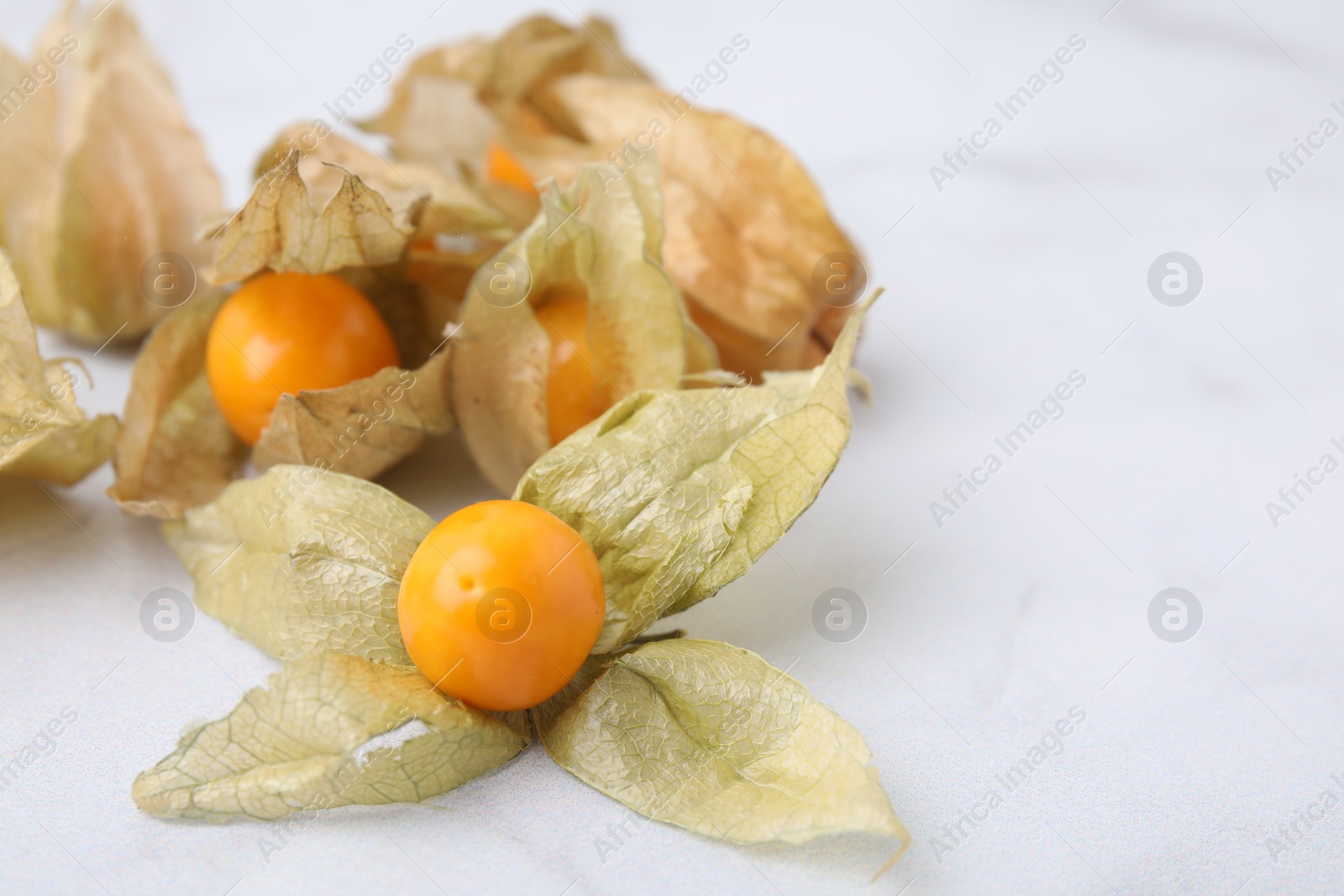 Photo of Ripe physalis fruits with calyxes on white marble table, closeup. Space for text