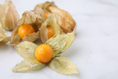 Ripe physalis fruits with calyxes on white marble table, closeup. Space for text