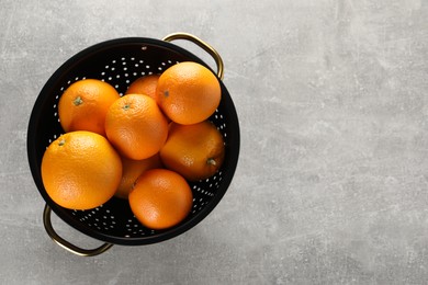 Photo of Fresh ripe oranges in black colander on light grey table, top view. Space for text