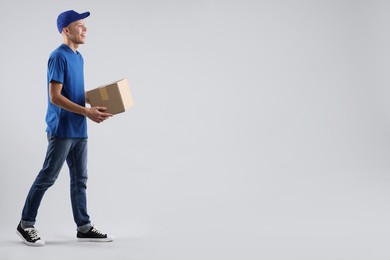 Photo of Happy courier with parcel on light grey background. Space for text