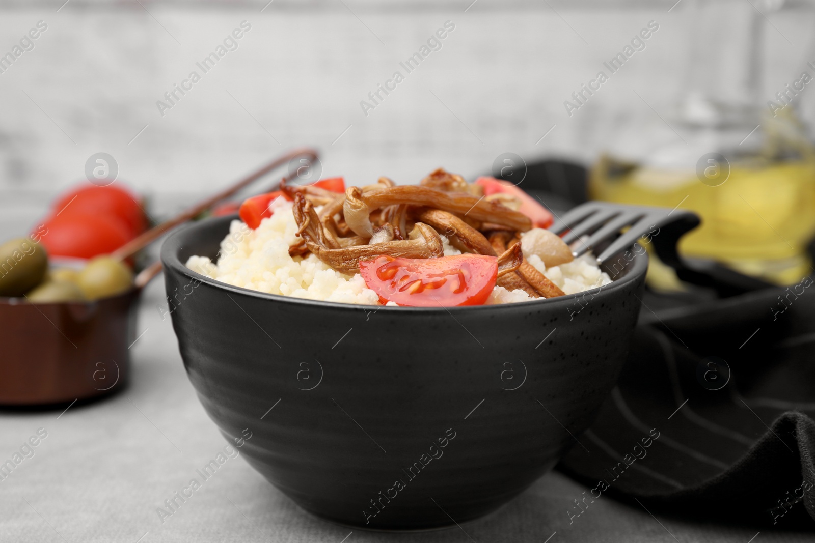 Photo of Tasty couscous with mushrooms and tomatoes on grey table, closeup