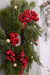 Photo of Beautiful Christmas wreath with red berries and decor hanging on white door, closeup