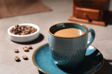 Delicious coffee with milk in cup and beans on light textured table, closeup. Space for text