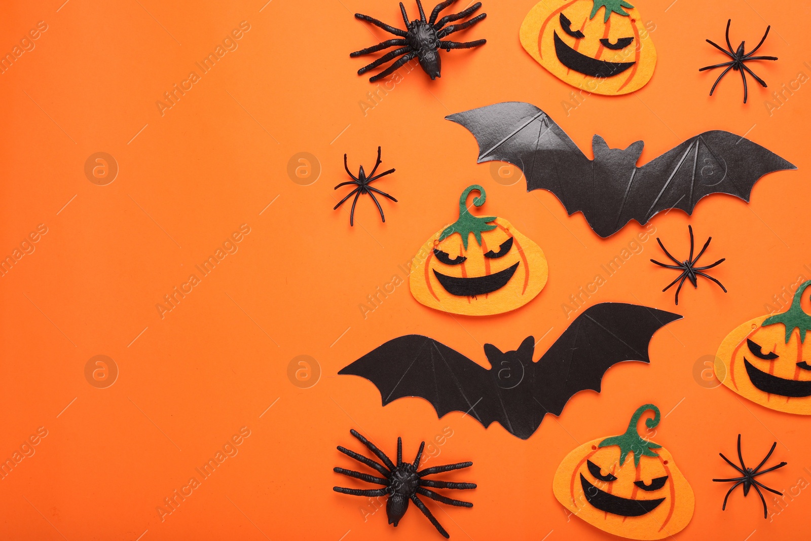 Photo of Flat lay composition with cardboard bats, felt pumpkins and spiders on orange background, space for text. Halloween celebration