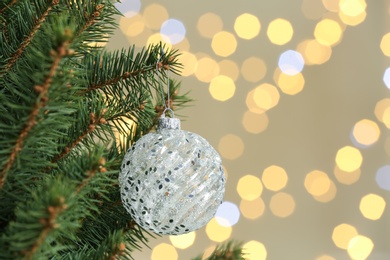 Photo of Holiday bauble hanging on Christmas tree against blurred lights. Space for text