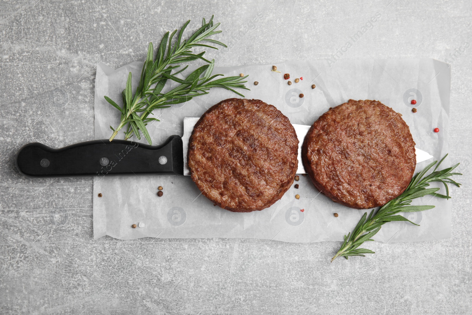 Photo of Tasty grilled hamburger patties, knife and seasonings on grey table, flat lay