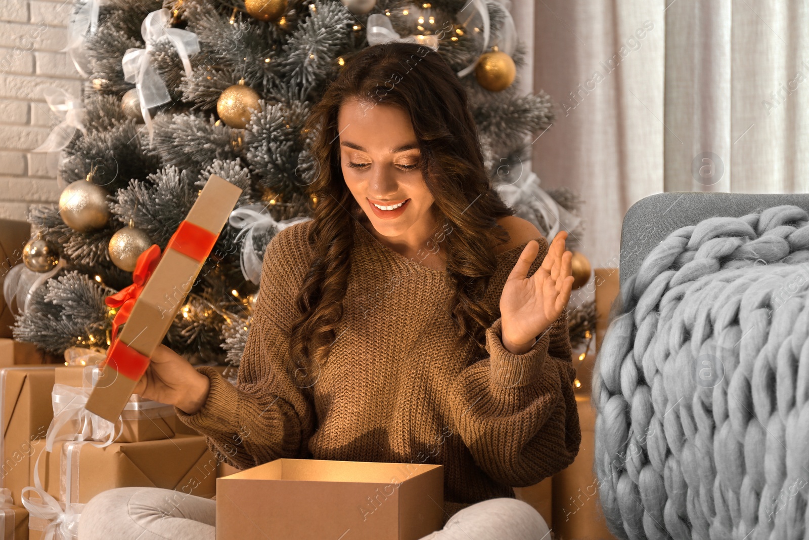 Image of Happy young woman opening Christmas gift at home. Magic holiday 