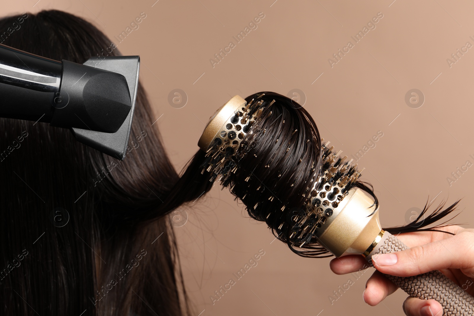 Photo of Hairdresser blow drying client's hair on light brown background, closeup