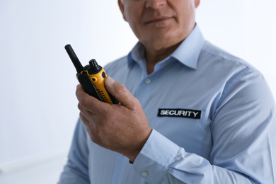 Photo of Professional security guard with portable radio set on light background, closeup