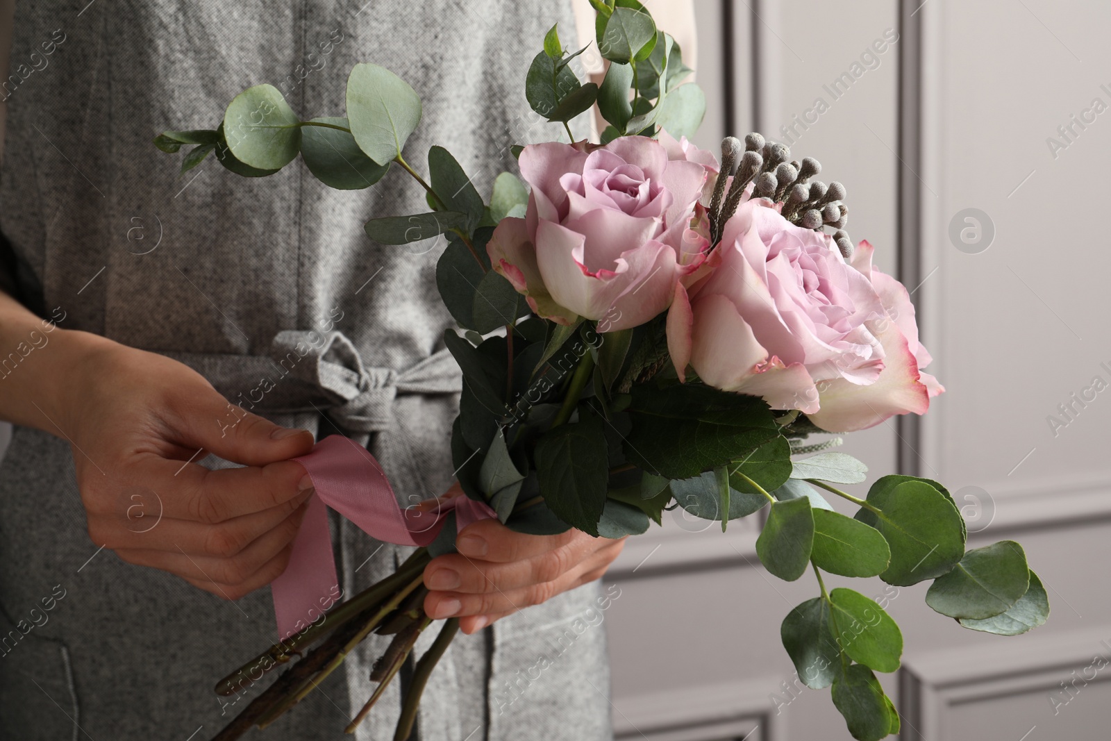 Photo of Florist creating beautiful bouquet at white wall, closeup