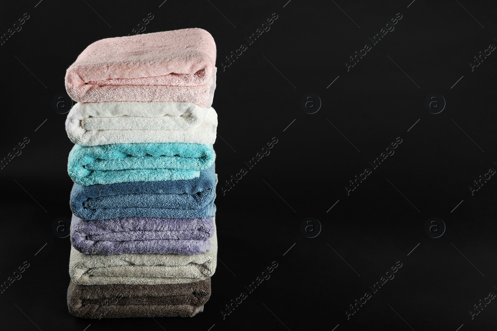 Photo of Different fresh soft terry towels on dark background. Space for text