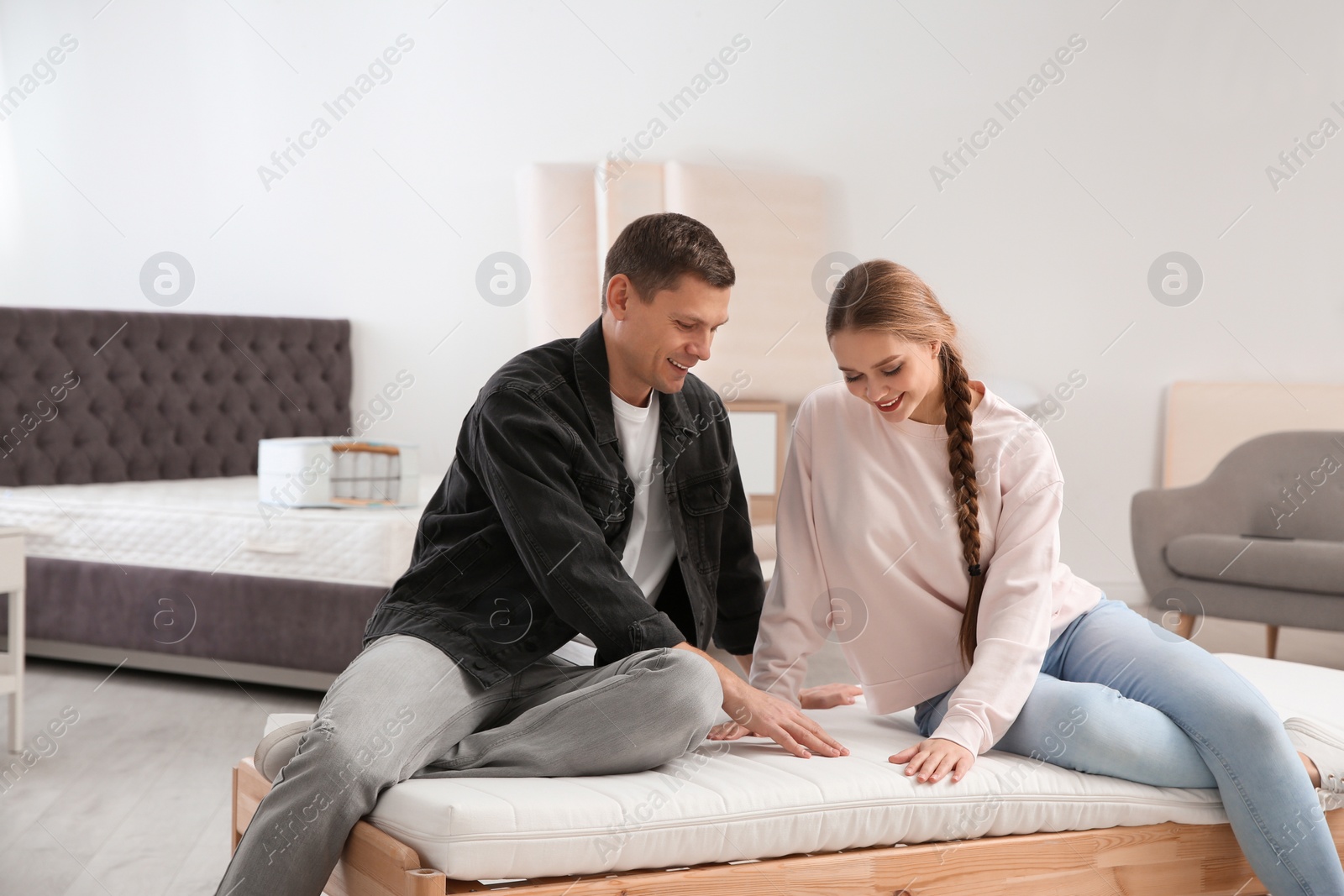 Photo of Happy couple choosing mattress in furniture store