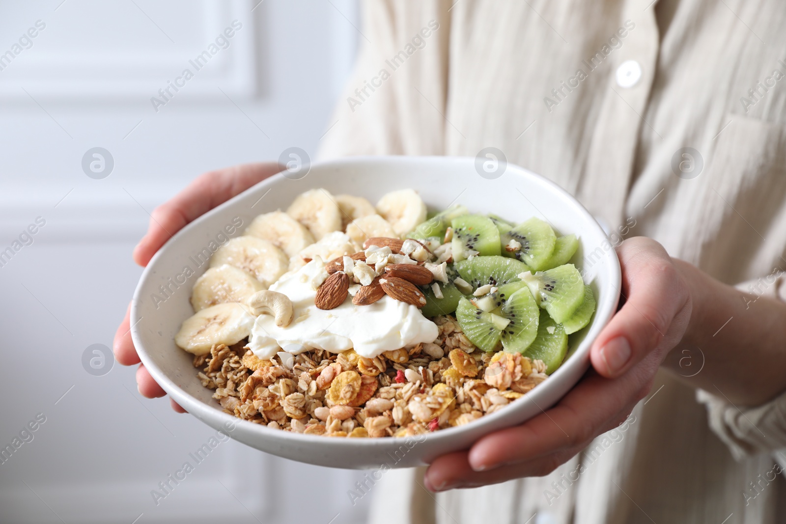 Photo of Woman holding bowl of tasty granola indoors, closeup