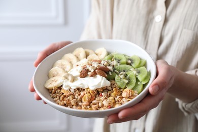 Woman holding bowl of tasty granola indoors, closeup