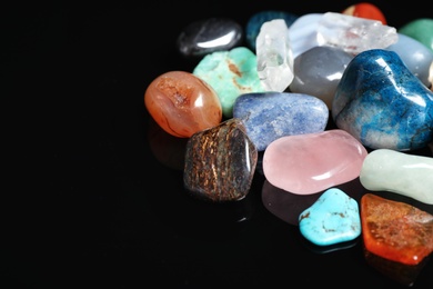 Different beautiful gemstones on black background, closeup. Space for text
