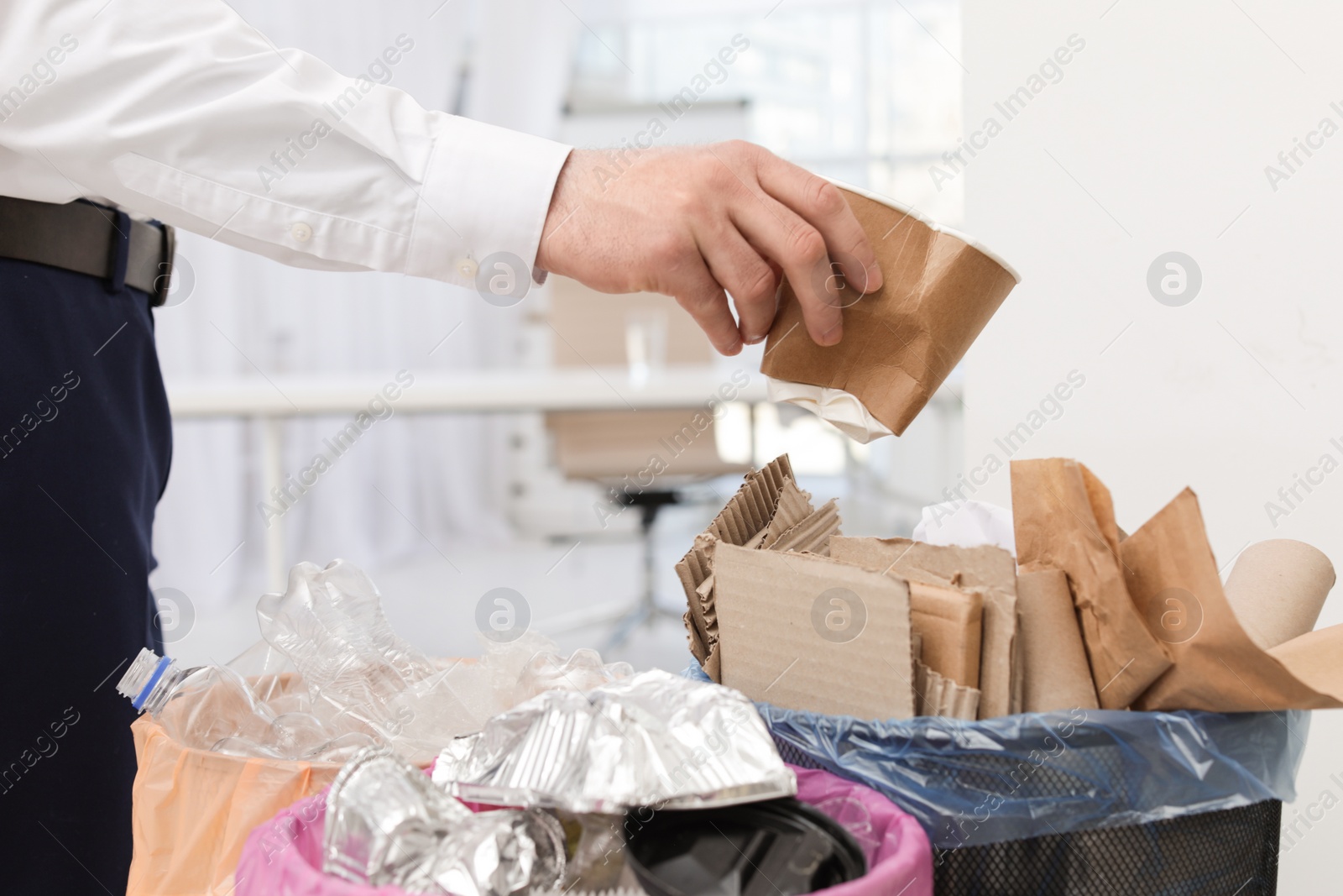 Photo of Man putting used paper cup into trash bin in office, closeup. Waste recycling