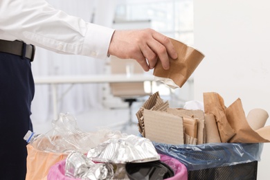 Man putting used paper cup into trash bin in office, closeup. Waste recycling