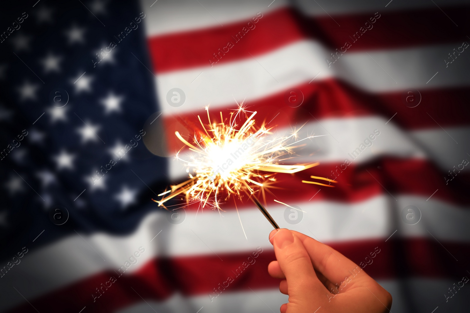 Image of 4th of July - Independence Day of USA. Woman holding burning sparkler against American flag, closeup