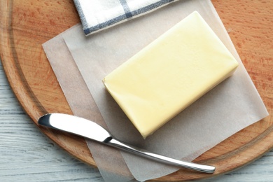 Wooden board with fresh butter and knife on table, top view