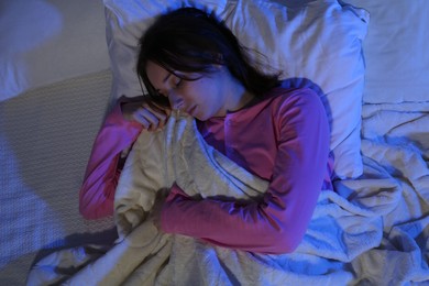 Photo of Young woman sleeping in soft bed at night, top view