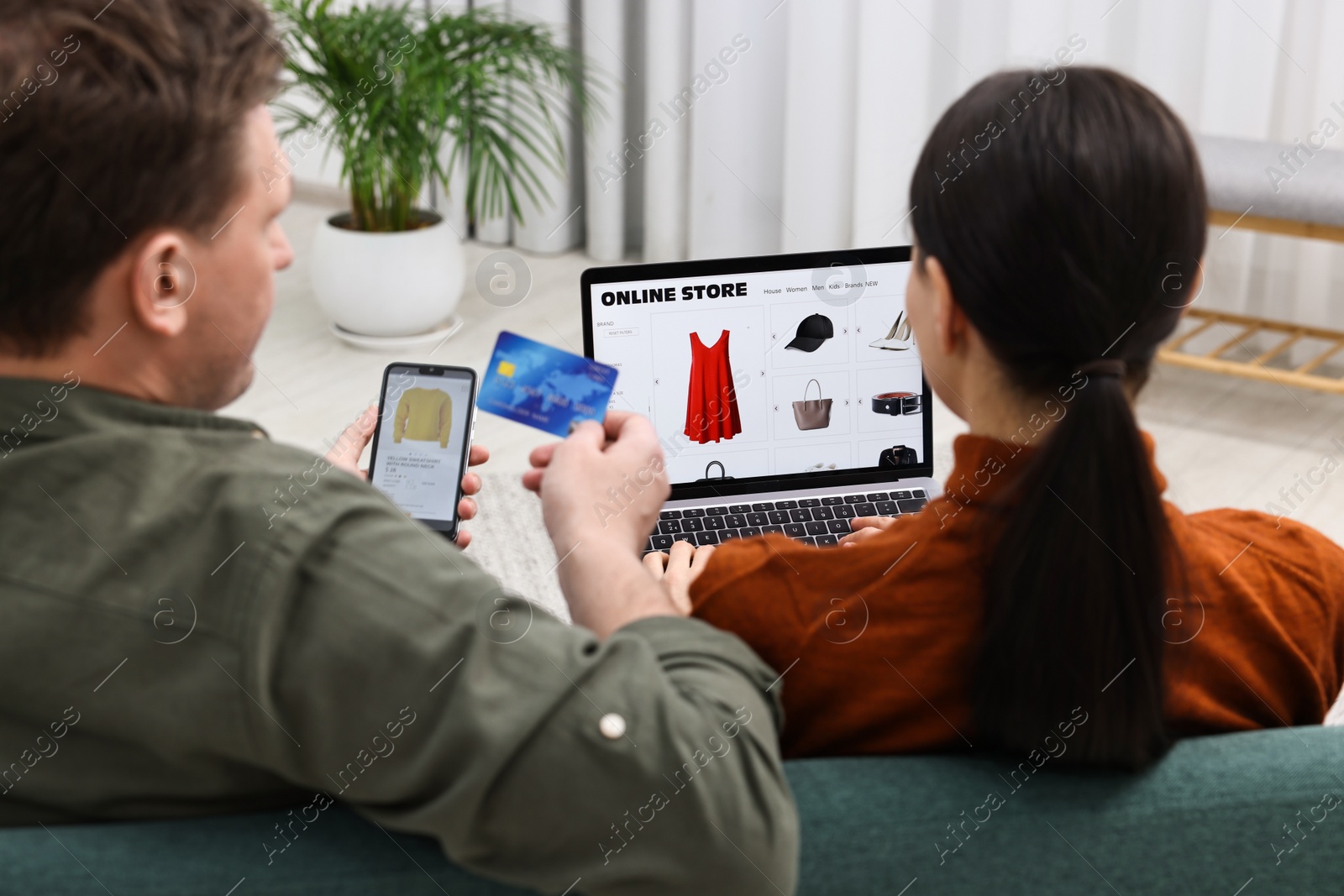 Photo of Couple with credit card and gadgets shopping online indoors, back view