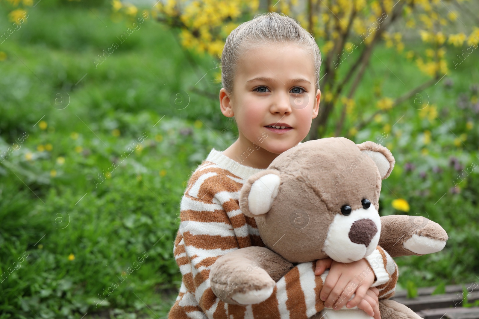 Photo of Little girl with teddy bear on wooden bench outdoors. Space for text