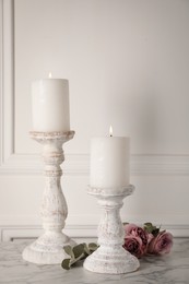 Elegant candlesticks with burning candles and flowers on white marble table